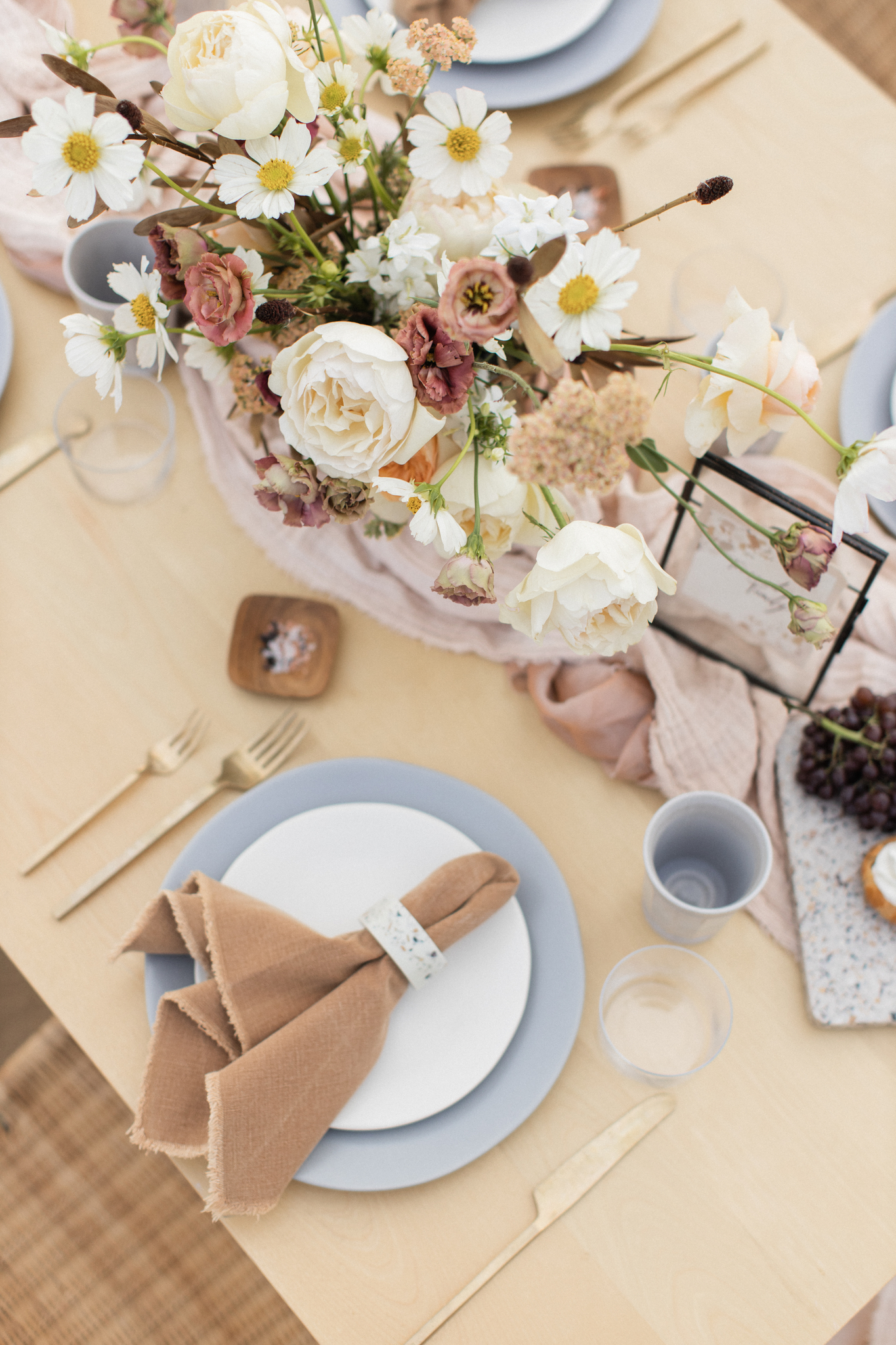 Elegant wedding planner-designed outdoor dining table setting with floral centerpiece, pastel dinnerware, and burlap napkins on a wooden table.
