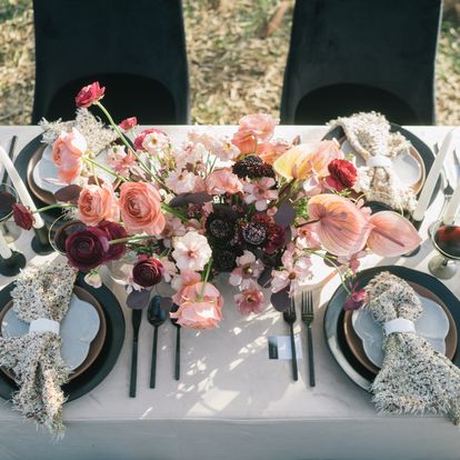 Elegant outdoor dining table setting with floral centerpieces, decorated plates, and cutlery, ready for a wedding event.