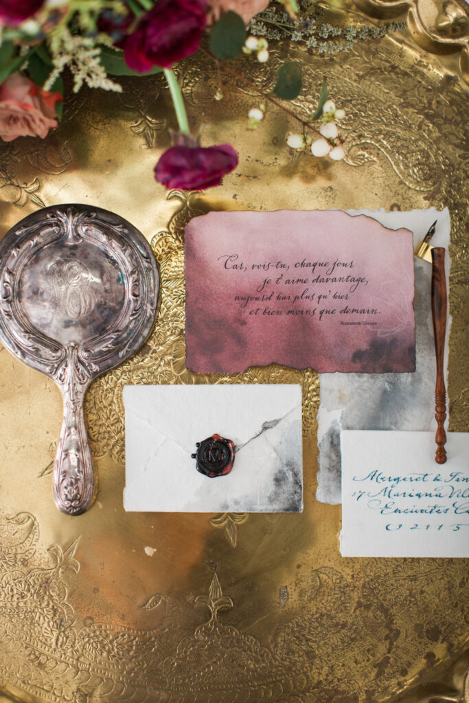 Vintage hand mirror and elegant wedding invitations with calligraphy and wax seal on a gold tray, curated by a top Charlotte wedding florist.