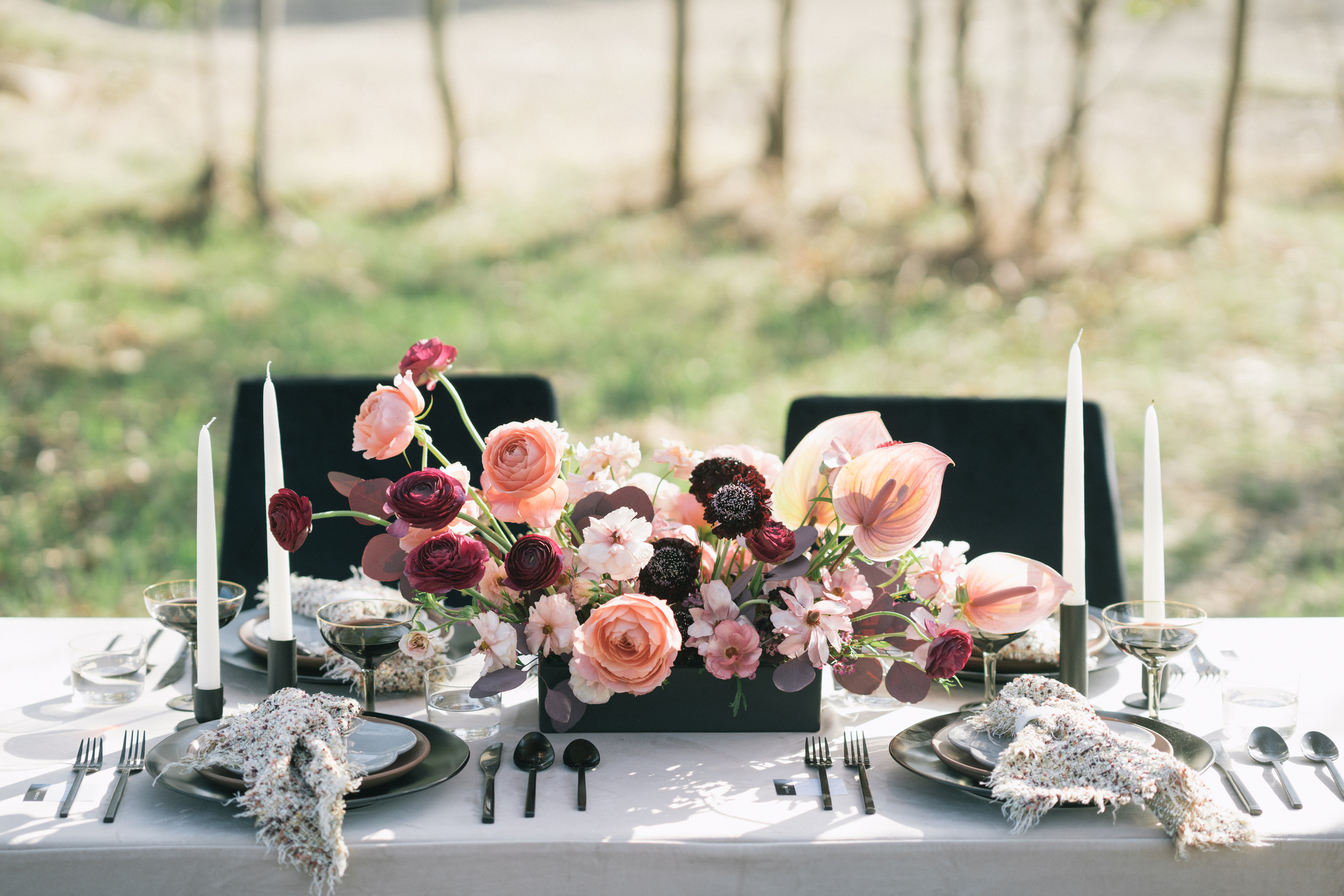 Elegant outdoor dining table setup with floral centerpiece by wedding florists Charlotte nc, black candles, and fine china in a sunlit garden setting.