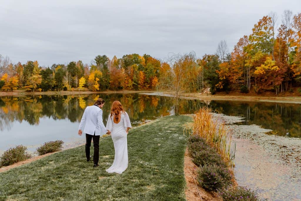 @nicklevinephoto_Abbey-Andrew-Preview_Splendor-Pond_Bride and Groom Walking along grass by Pond at Mooresville Wedding Venue