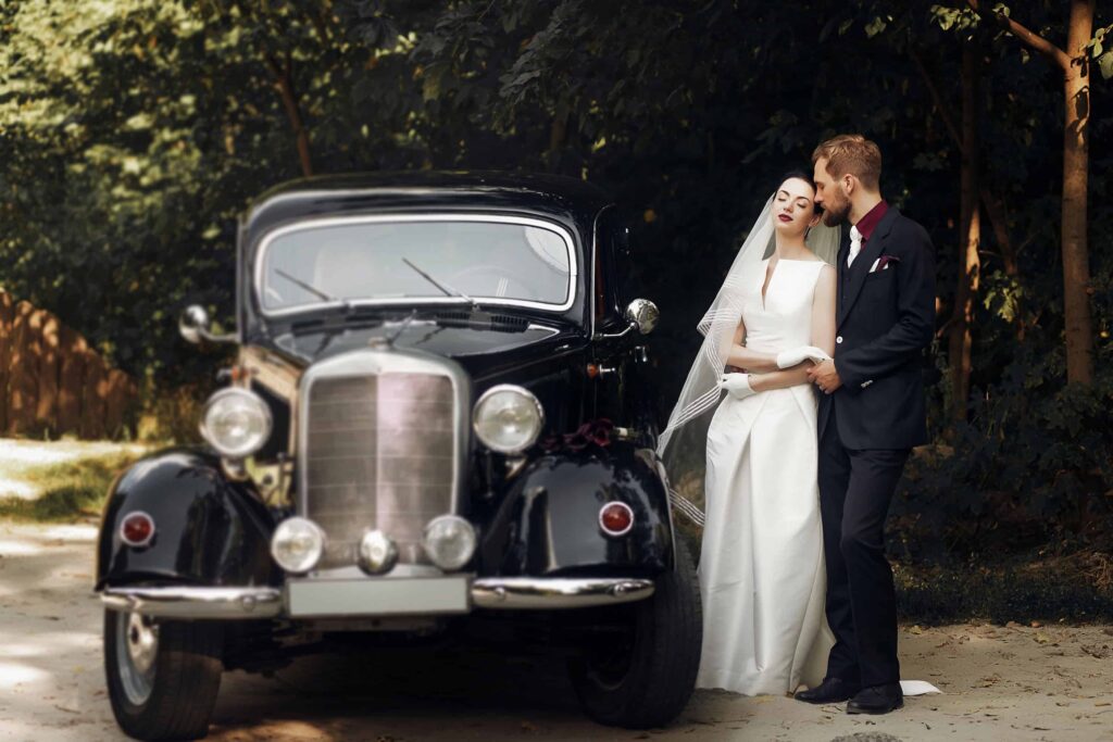 luxury elegant wedding couple holding hands on background of stylish black car . gorgeous bride and handsome groom in retro style. romantic moment