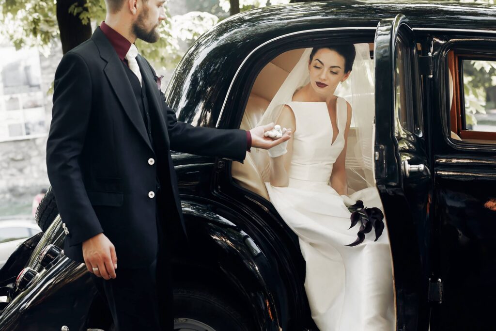 elegant handsome stylish groom helping gently gorgeous bride, holding hand. unusual luxury wedding couple in retro style. romantic moment