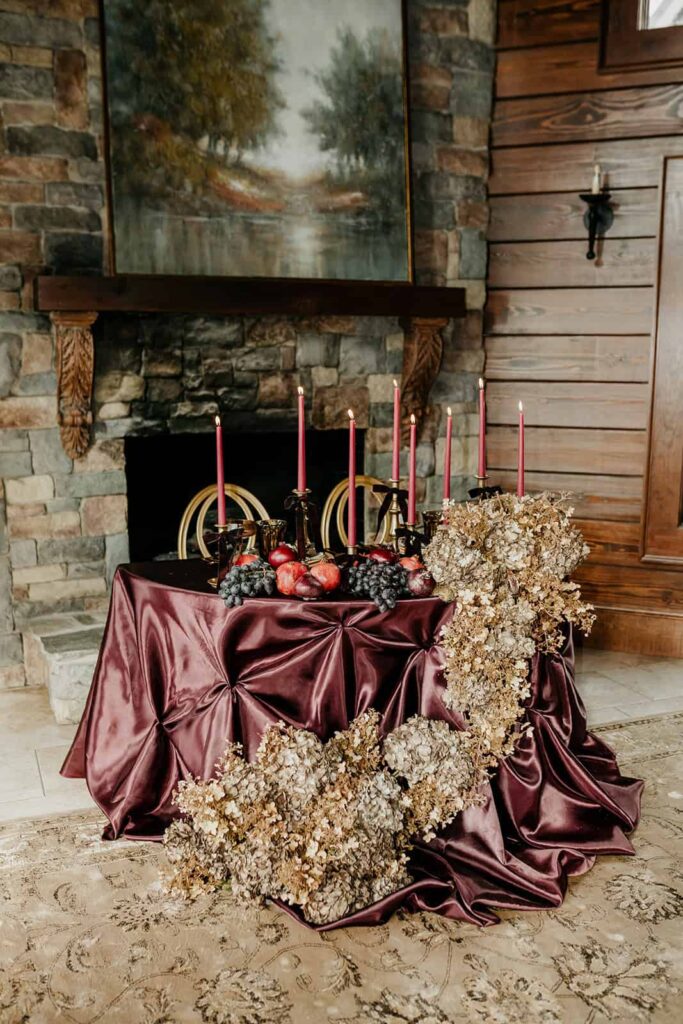 Sunset Ridge Estate luxury southern wedding venue in Monroe NC with moody winter sweetheart table in front of fireplace at large estate with gold candles and large florals and fruit in shades of chocolate brown and burgundy by Crafted Charm Florals