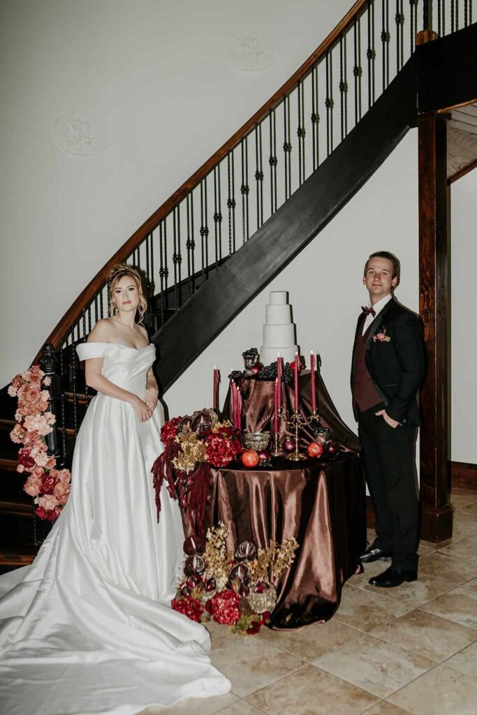 Sunset Ridge Estate luxury southern wedding venue in Monroe NC with bride and groom cake cutting at moody winter sweetheart table in front of grand stairs at large estate for newlywed portraits