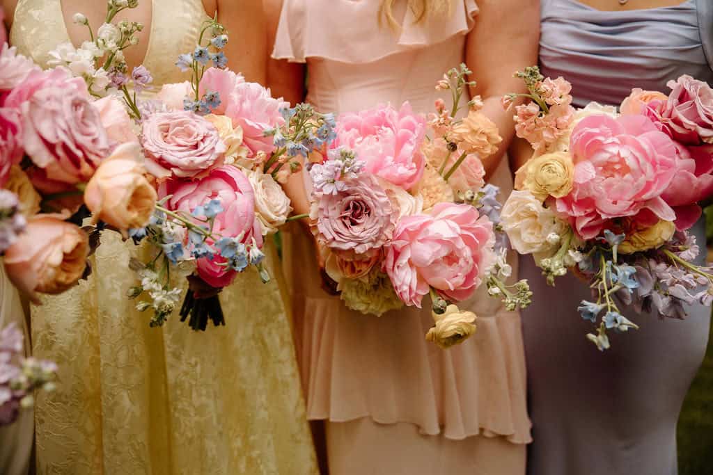 Spring florals by Crafted Charm Florals with bridesmaids holding bouquets of roses, peonies, ranunculus, delphinium.
