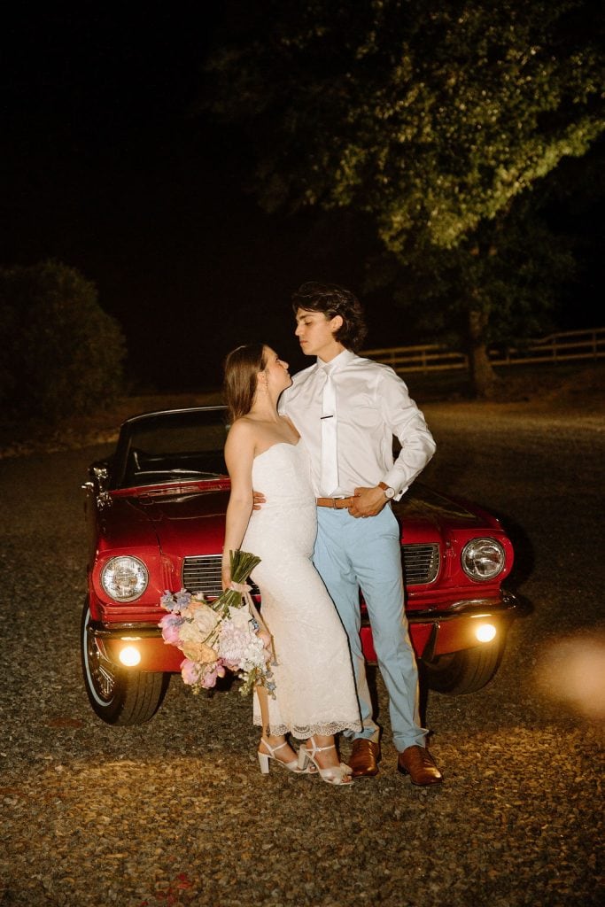 bride and groom portrait with bride carrying large floral bouquet of spring colors and peonies at the Historic Robertson Homestead in Rock Hill, SC, in front of a getaway car colored red