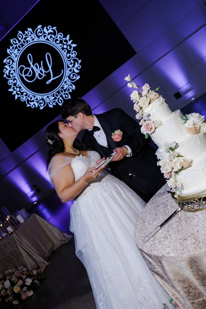 Bride and groom cutting cake at The Revelry Charlotte NC wedding venue decorated in luxury florals with gold and soft pink accents by Crafted Charm Florals